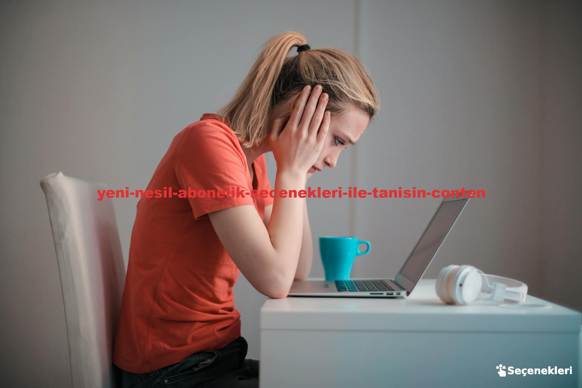 A woman sits indoors at a table, looking concerned while using a laptop with headphones and a coffee mug nearby.